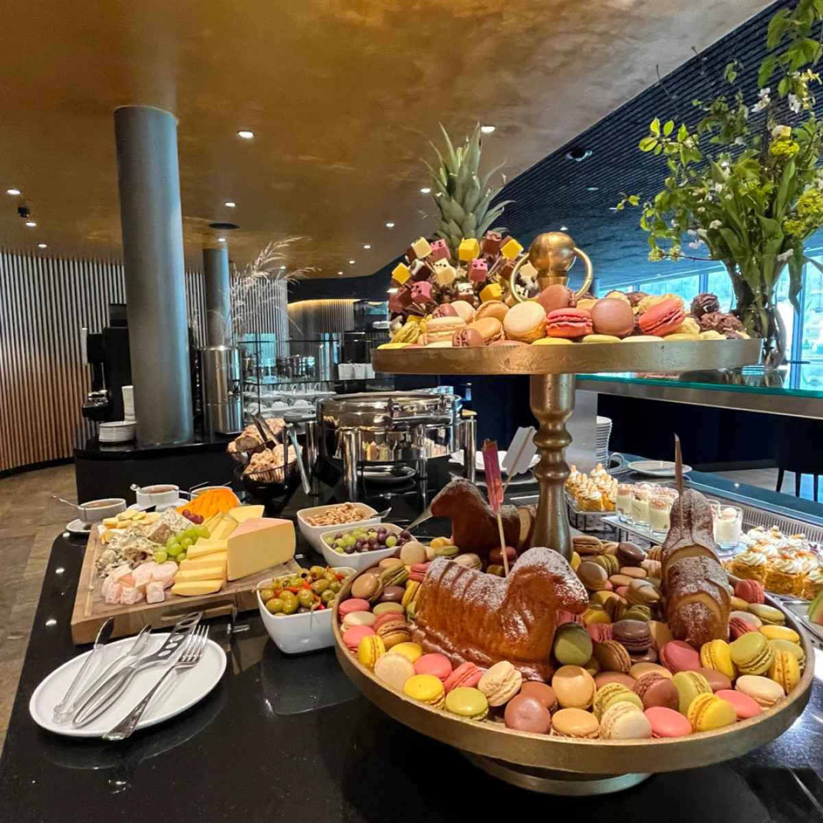 Ein luxuriöses Buffet mit einer Vielfalt an Speisen: Macarons in verschiedenen Farben, Käse, Obst, Häppchen und eine dekorative Obstschale. Elegante Präsentation in einem stilvollen Ambiente.